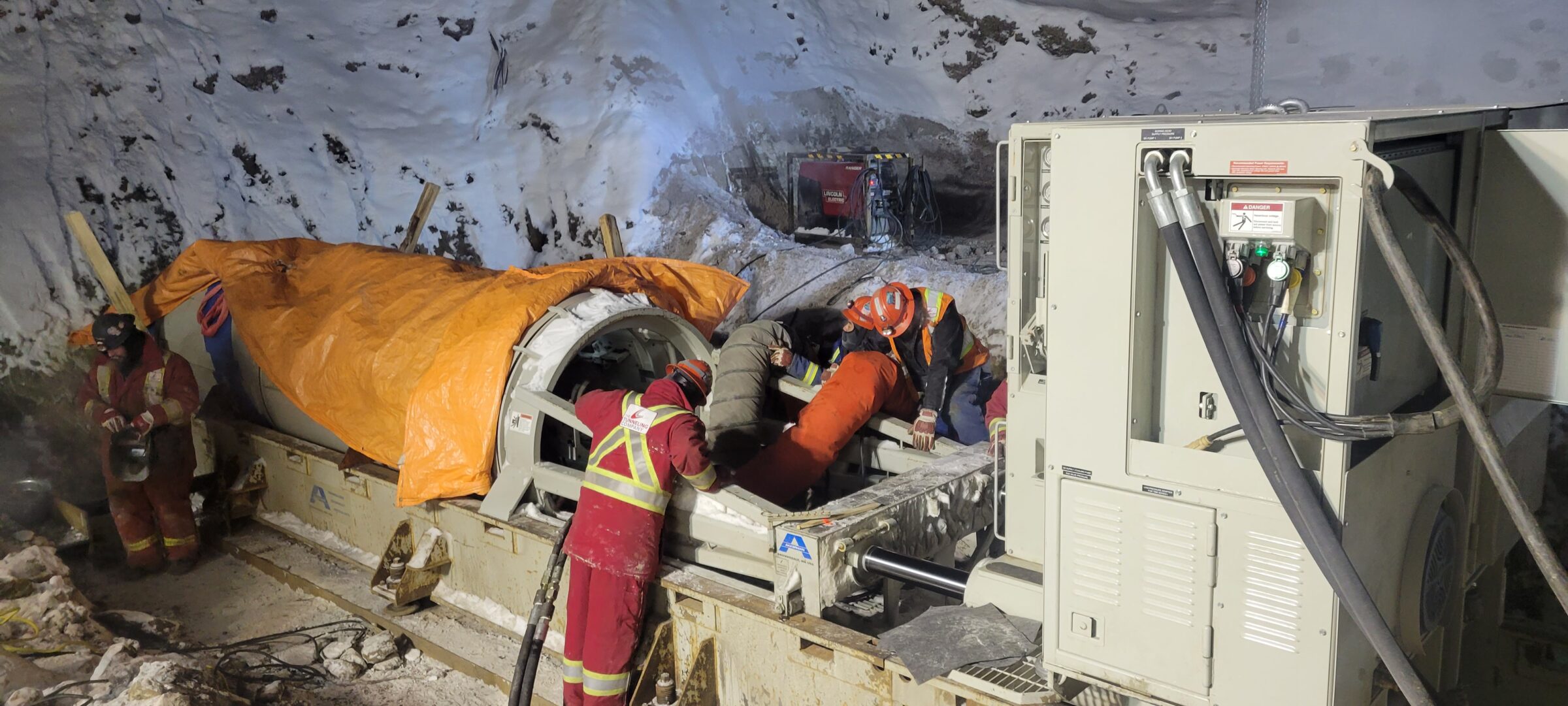 Construction crew operating pipe jacking and tunnel boring equipment at a snowy excavation site in Inuvik, Canada.