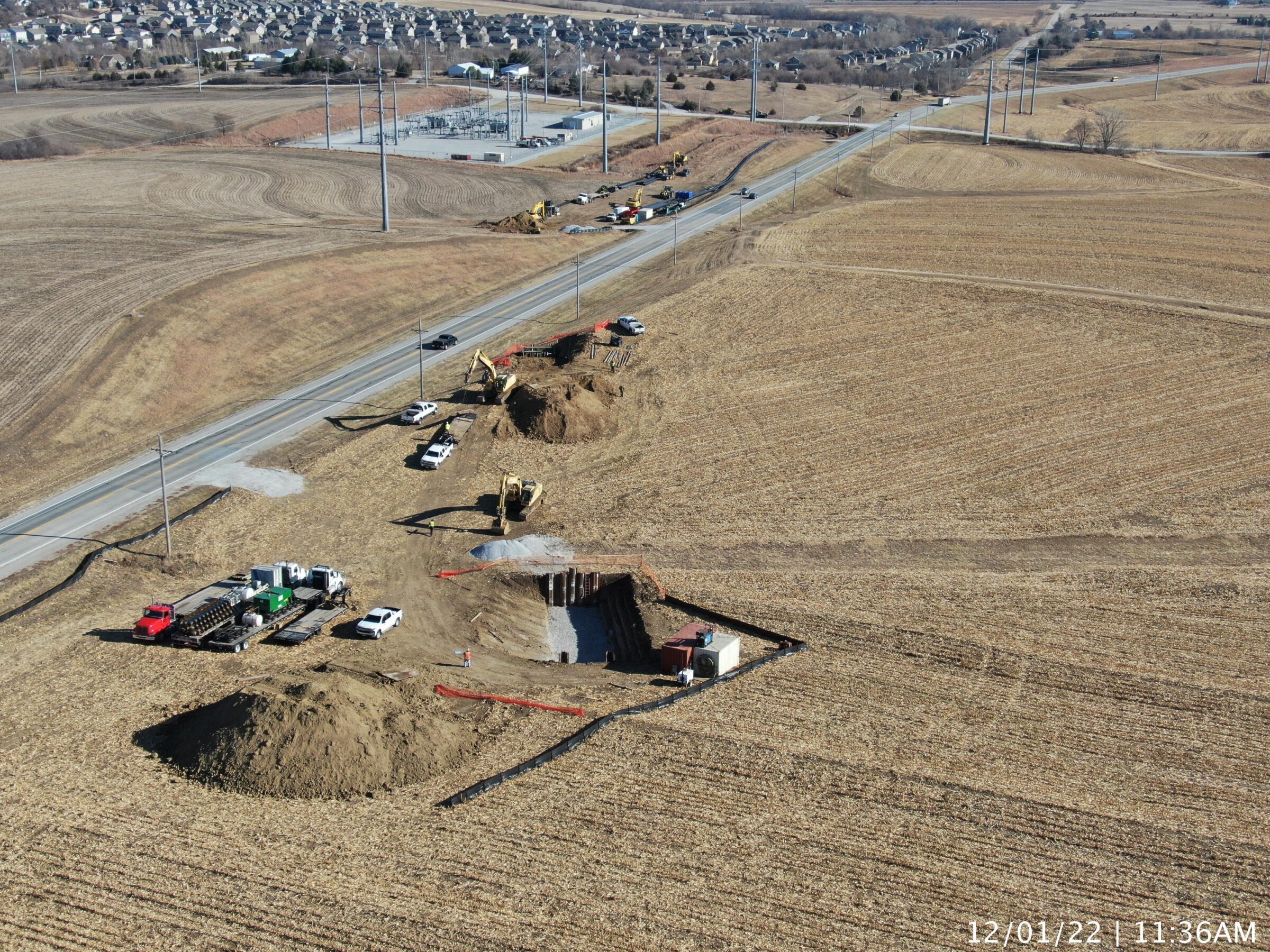 Aerial view of a trenchless construction site with excavated pits, equipment, and vehicles along a rural roadway surrounded by farm fields.