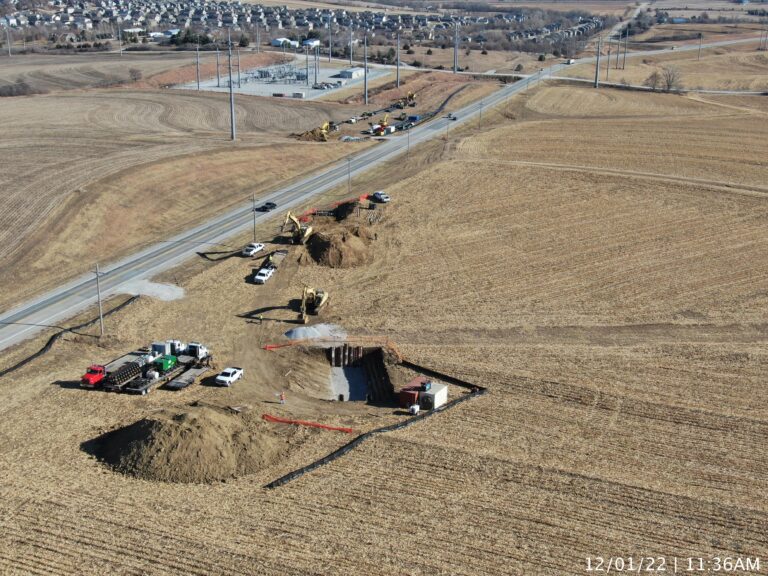Aerial view of a trenchless construction site with excavated pits, equipment, and vehicles along a rural roadway surrounded by farm fields.