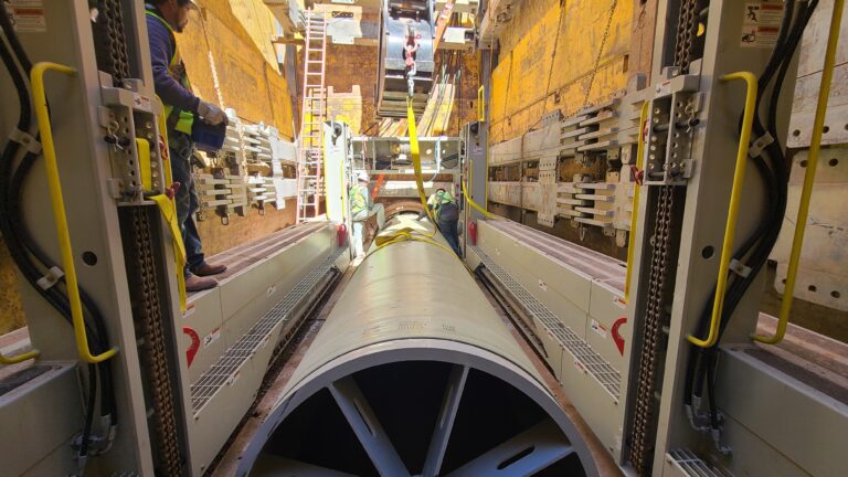 Large pipe section being positioned inside a construction trench during a sliplining installation.