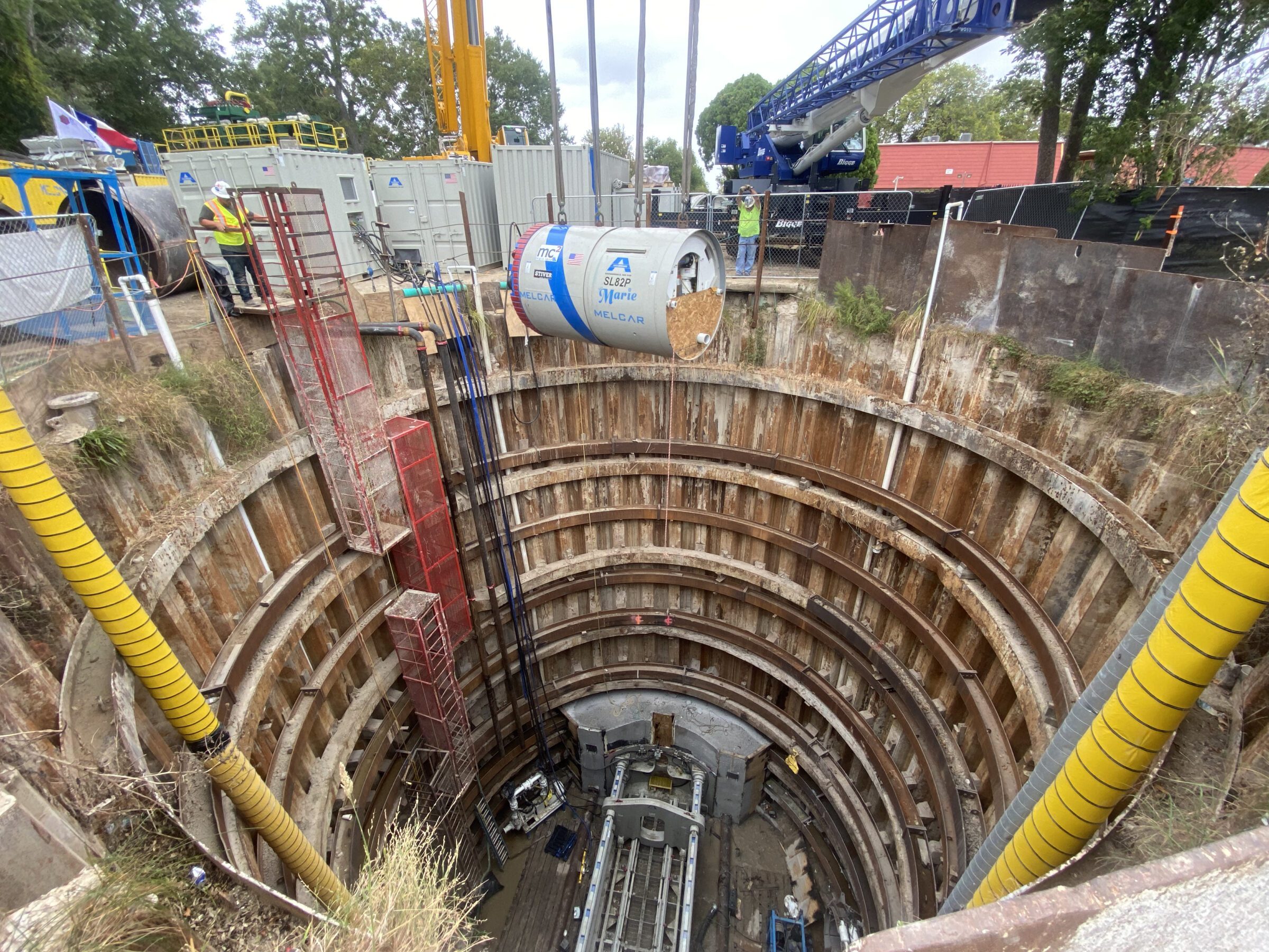 Large circular excavation shaft with microtunneling equipment being lowered by crane at a construction site.