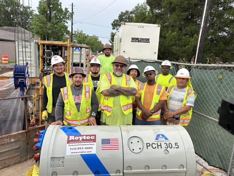 Construction crew standing behind microtunneling equipment at an active trenchless construction site.
