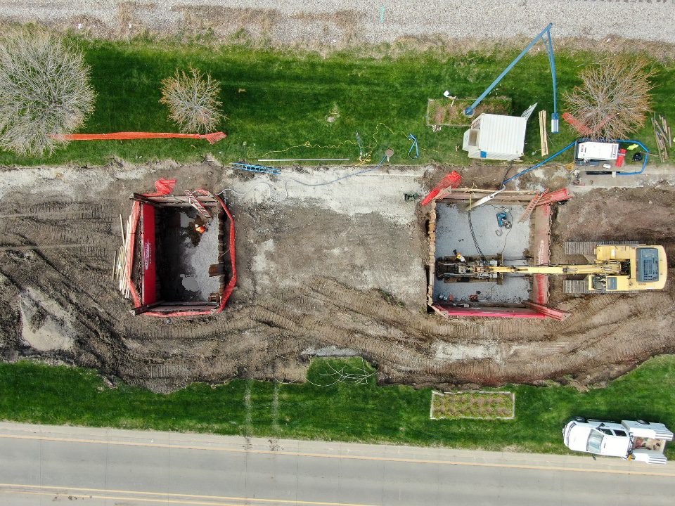 Aerial view of a trenchless construction site with two excavation pits, equipment, and vehicles along a roadway.