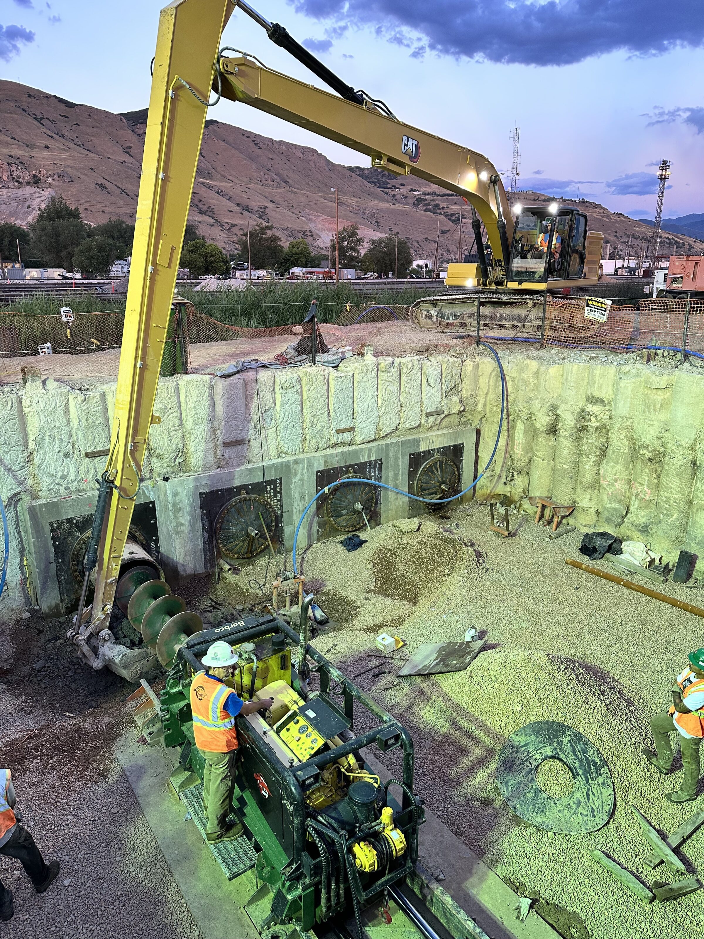 Excavator and auger boring equipment operating inside a large excavation pit at a trenchless construction site.